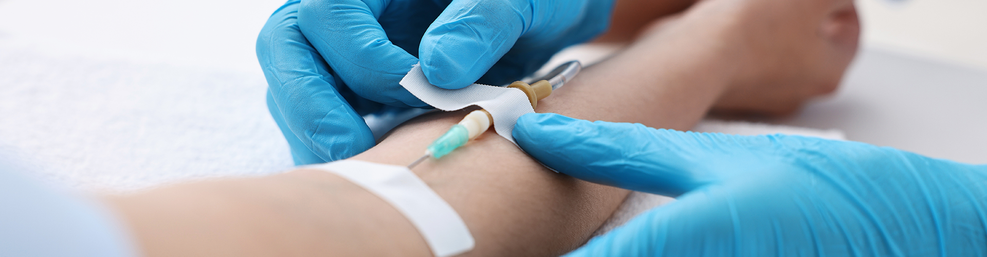 Gloved hands taping down IV needle to person's arm.